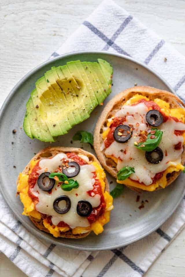 Breakfast English Muffin Pizzas on a plate with sliced avocados