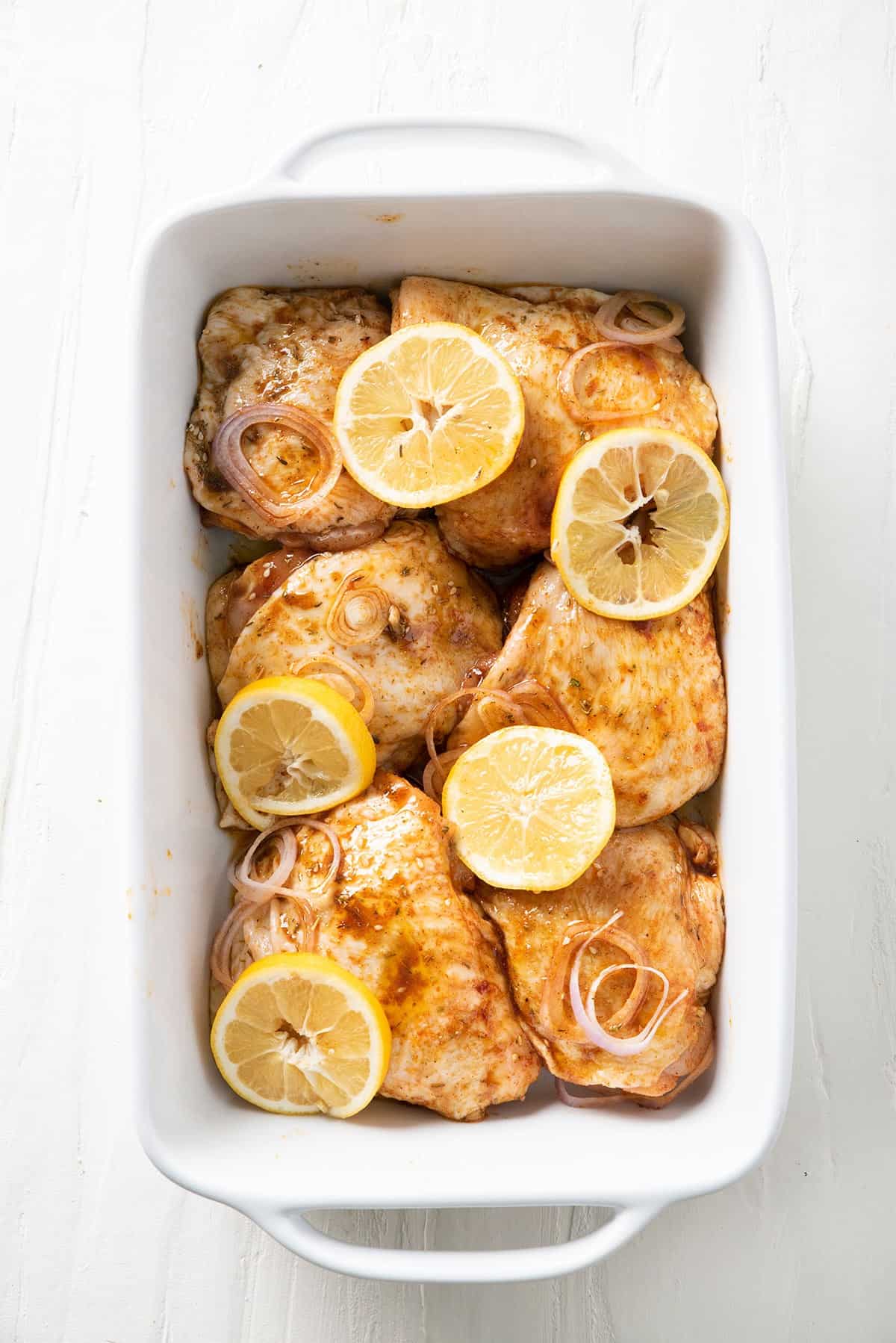 Chicken, shallots, and lemons added to a baking dish.