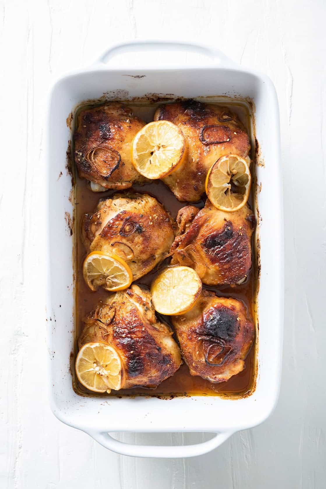 Chicken, shallots, and lemons in a baking dish after cooking and removing from oven.