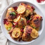 Pomegranate chicken thighs in a serving bowl with shallots, lemons, and garnish.