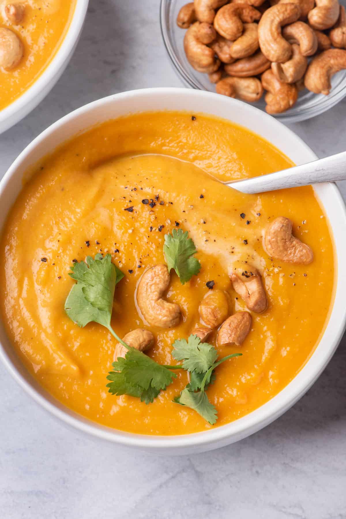 Spoon scooping bite of sweet potato soup garnished with cashews and cilantro
