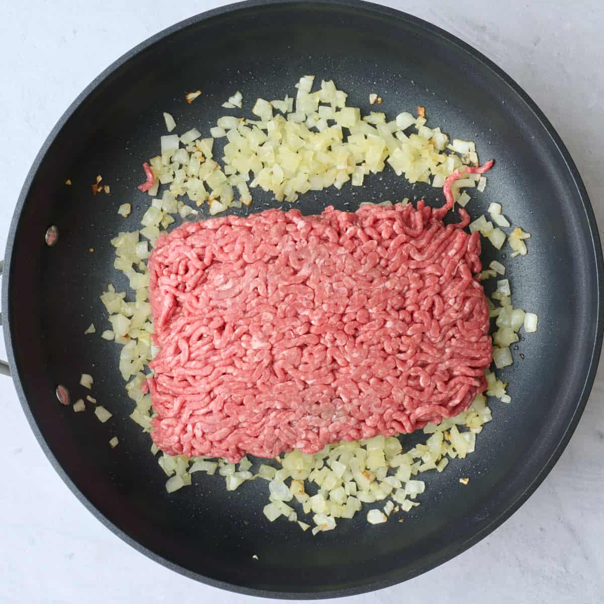 Cooked onions in a large skillet with raw ground beef added.