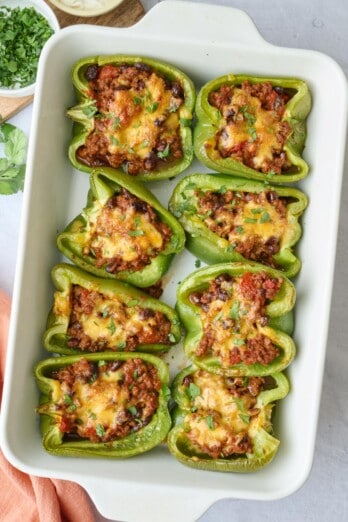 Taco stuffed bell peppers in the baking dish at a slight angle, garnished with chopped cilantro and a small dish of sour cream with spoon dipped inside nearby.