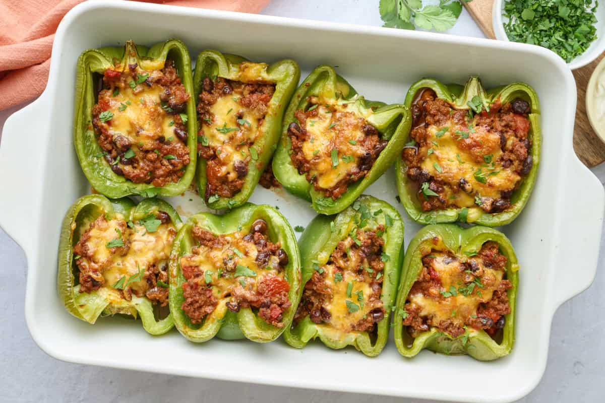 Taco stuffed bell peppers in the baking dish at a slight angle, garnished with chopped cilantro and a small dish of sour cream with spoon dipped inside nearby.