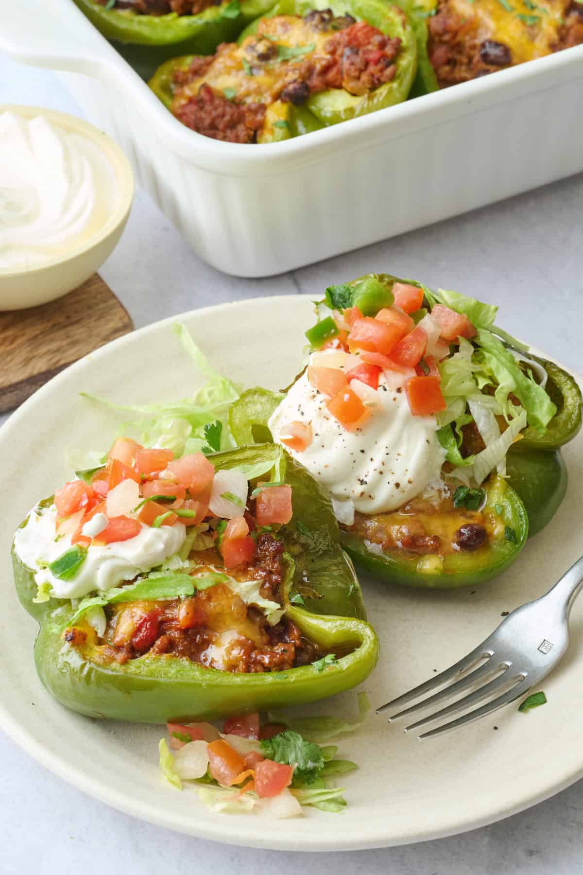 2 stuffed pepper halves on a small plate with, topped with sour cream and lettuce.