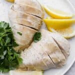 Poached chicken on plate with lemon slices and herbs