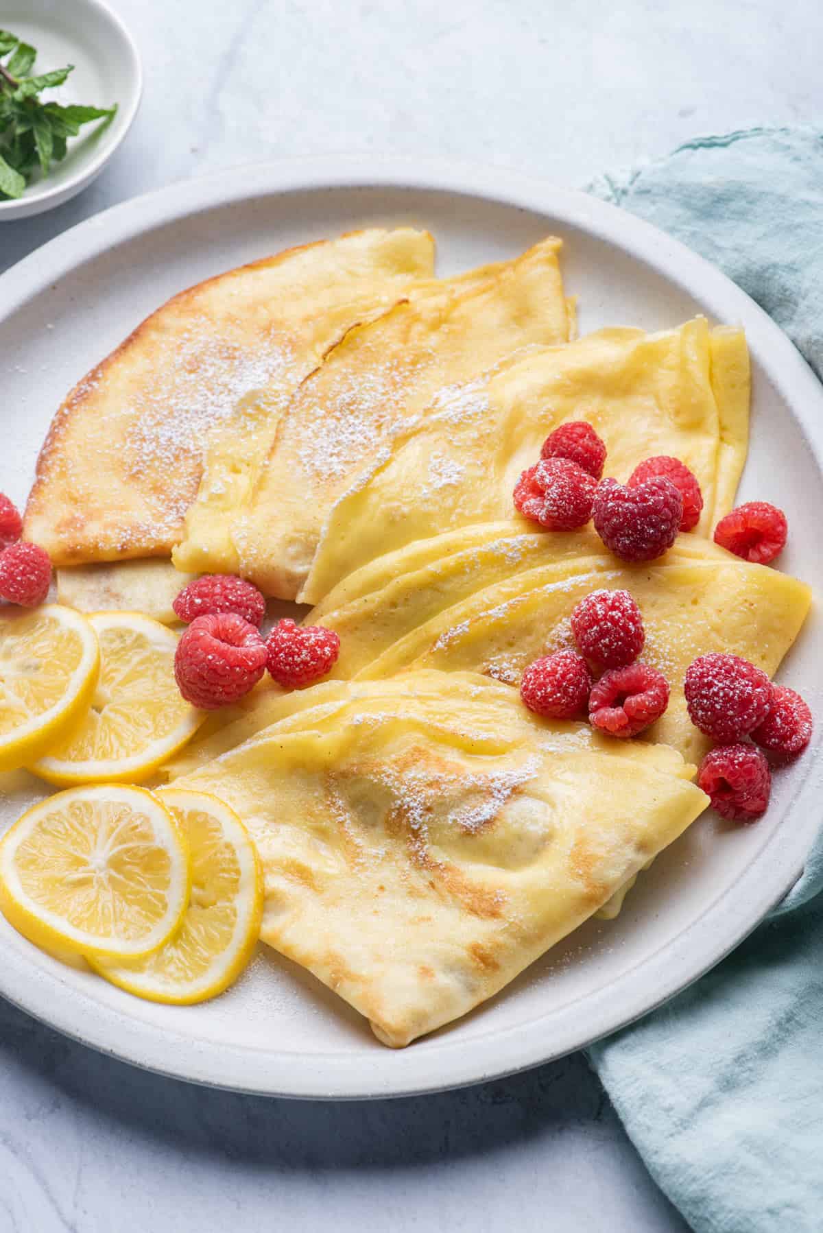 Close up of crepes on plate with raspberries and lemon