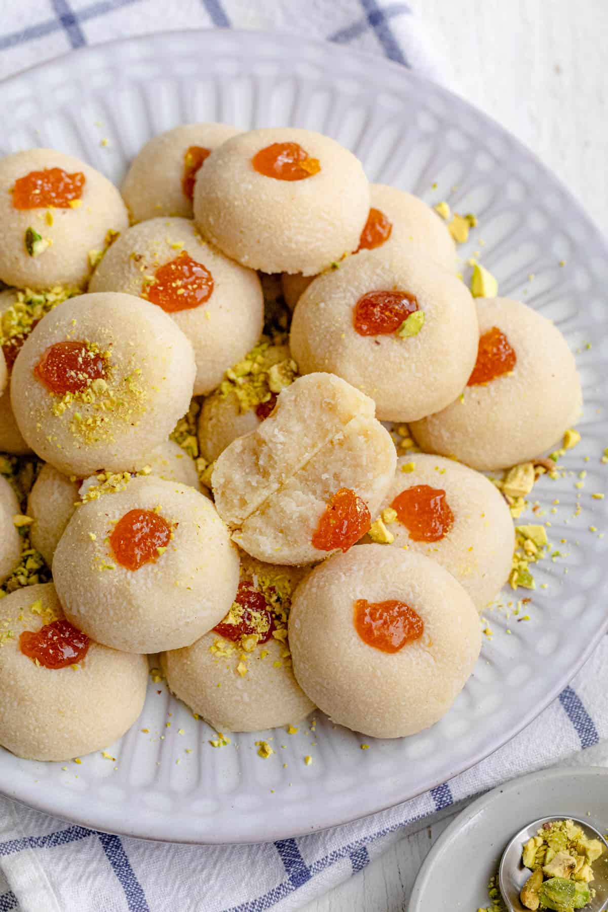 Plate of ghraybeh cookies with jam in the middle with of the cookies cut in half to show texture