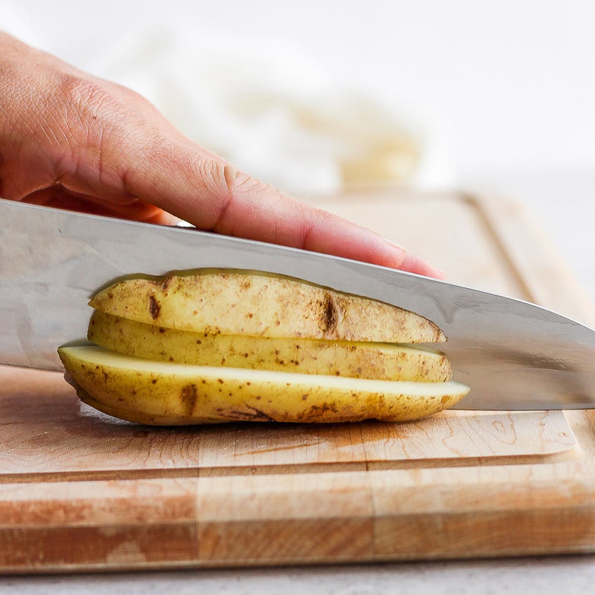 Slicing small slices lengthwise, with the potato sitting on the previously cut surface.
