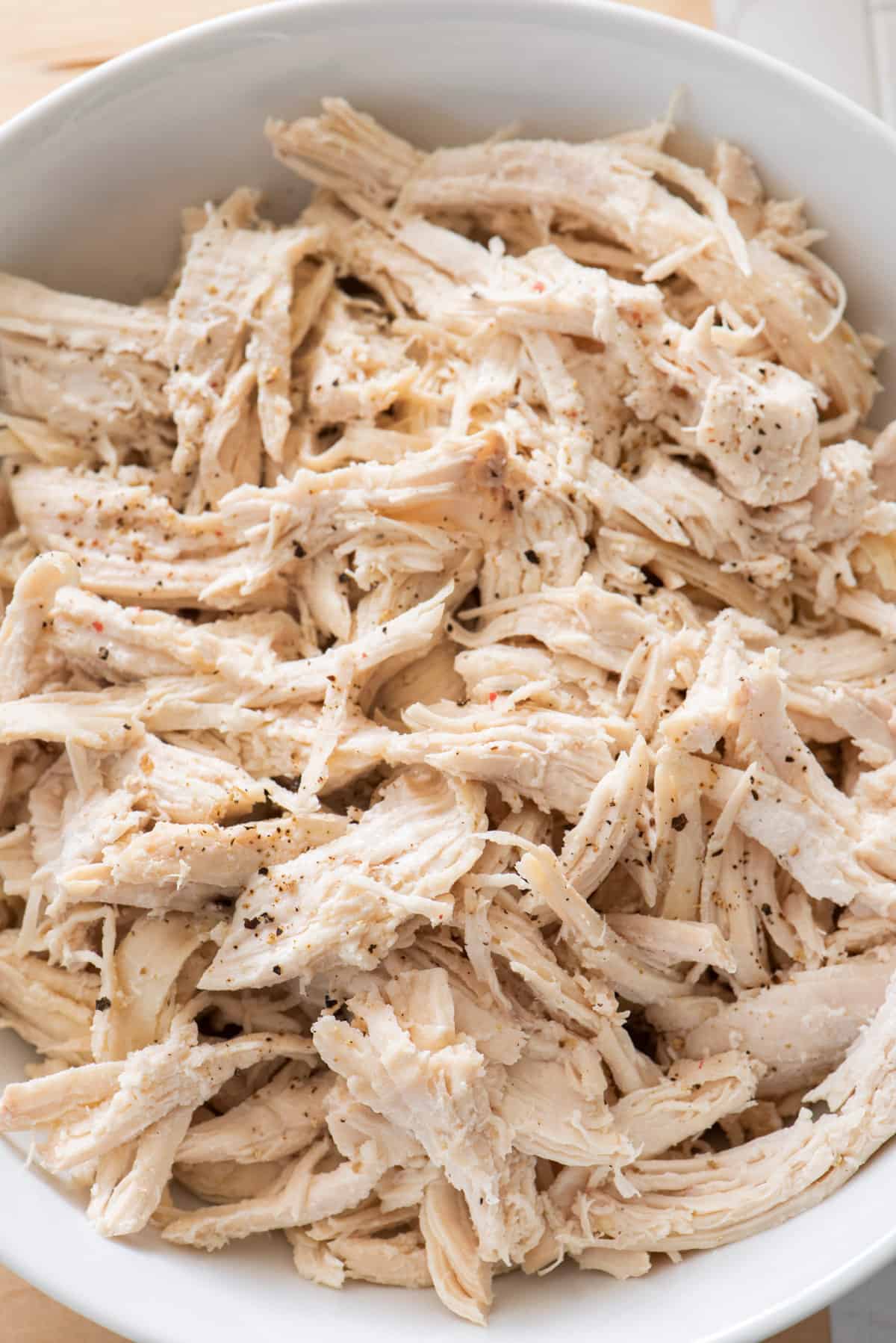 Close up for shredded chicken in a large white bowl