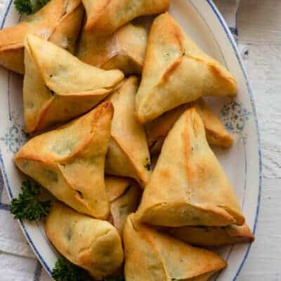 Large platter of spinach pies with small bowl of yogurt for dipping