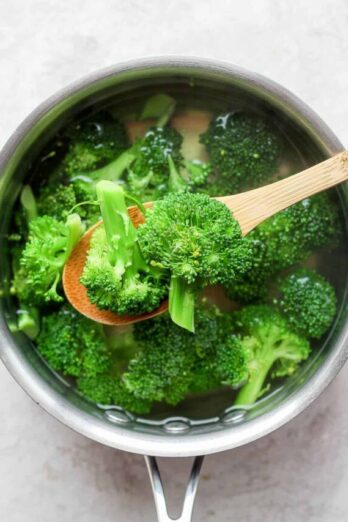 Cooked broccoli on slotted wooden spoon over pot of broccoli cooking