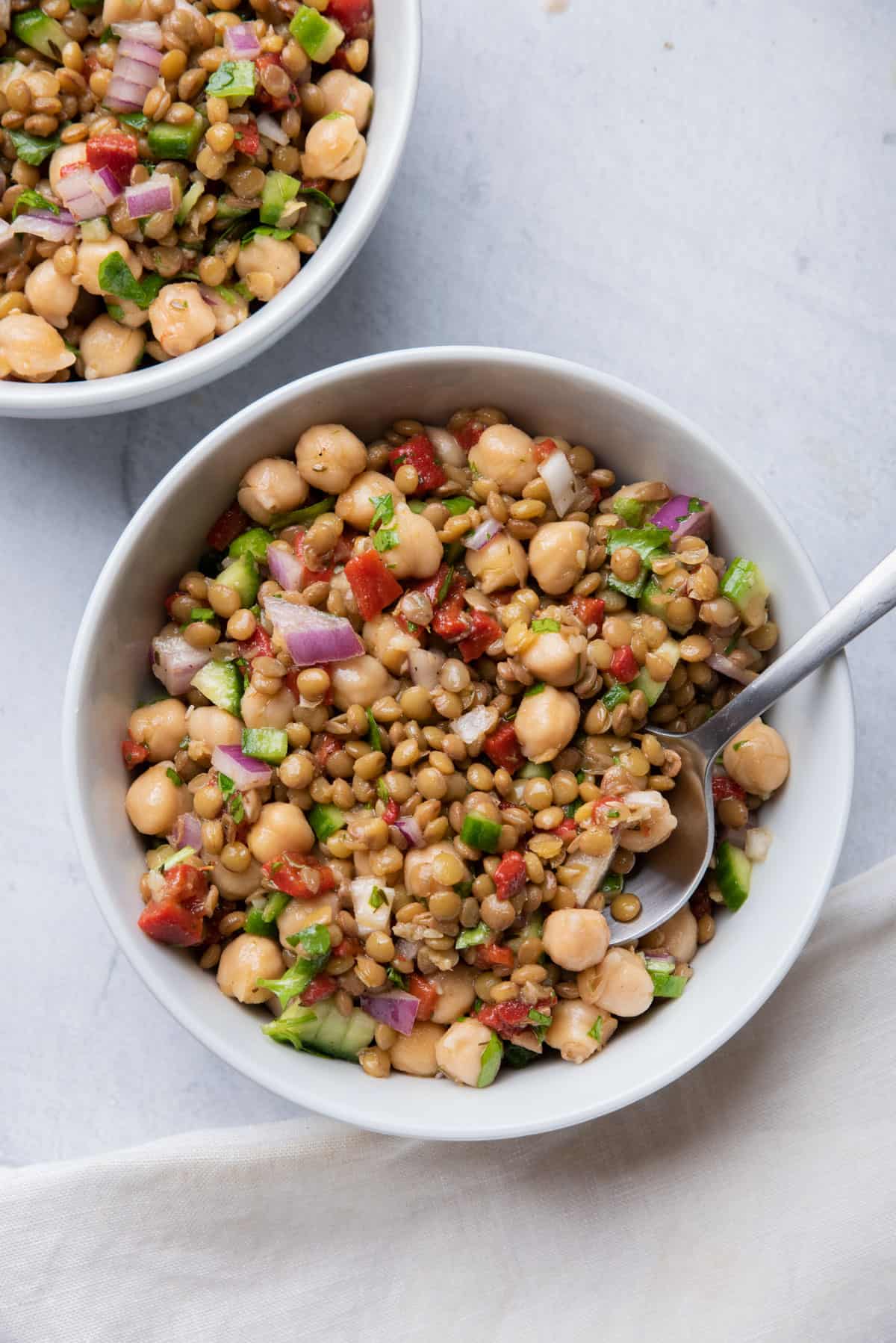 Two small bowls of lentil salad with spoon inside of one