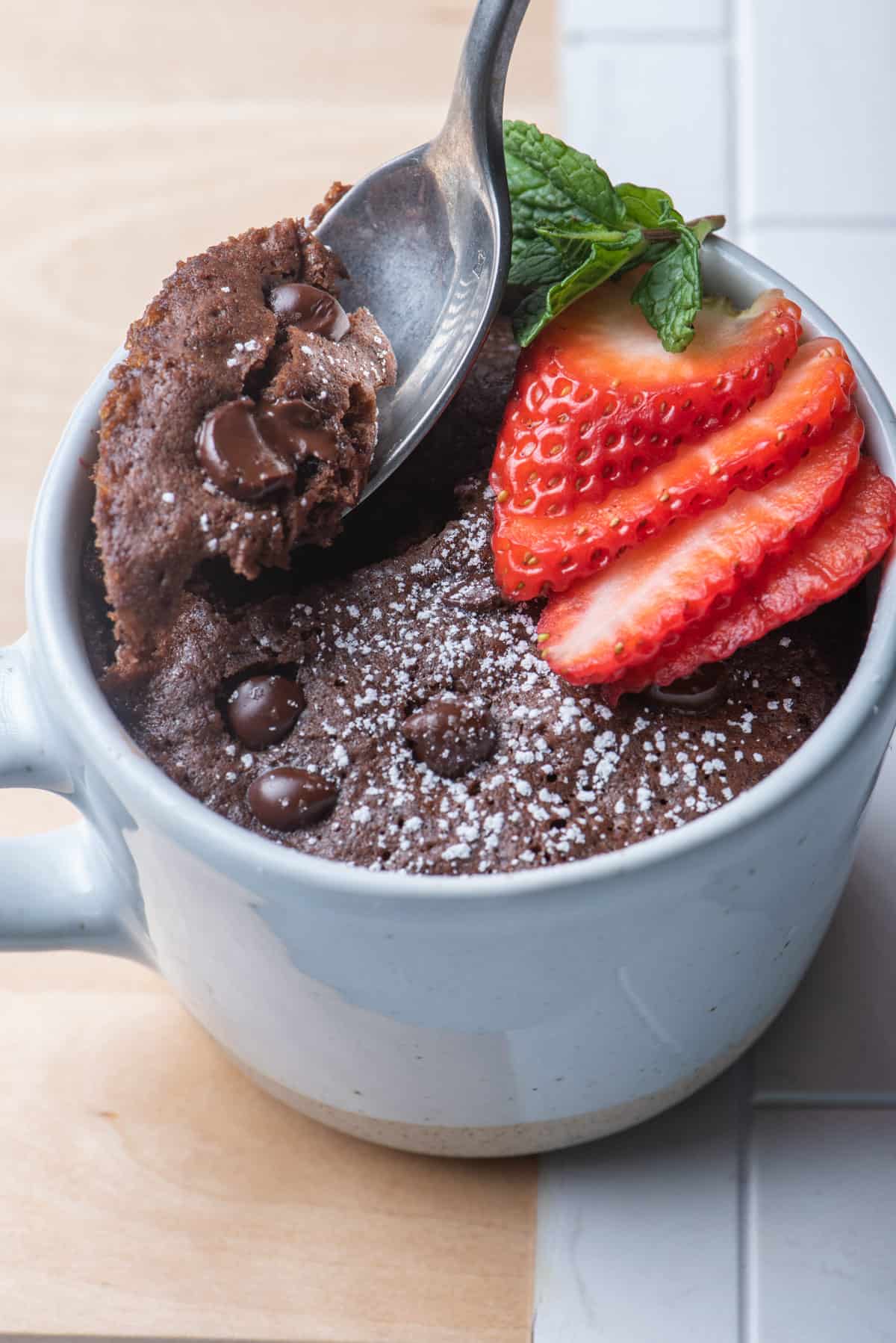 Spoon taking bite out of chocolate mug cake with strawberry slices on top