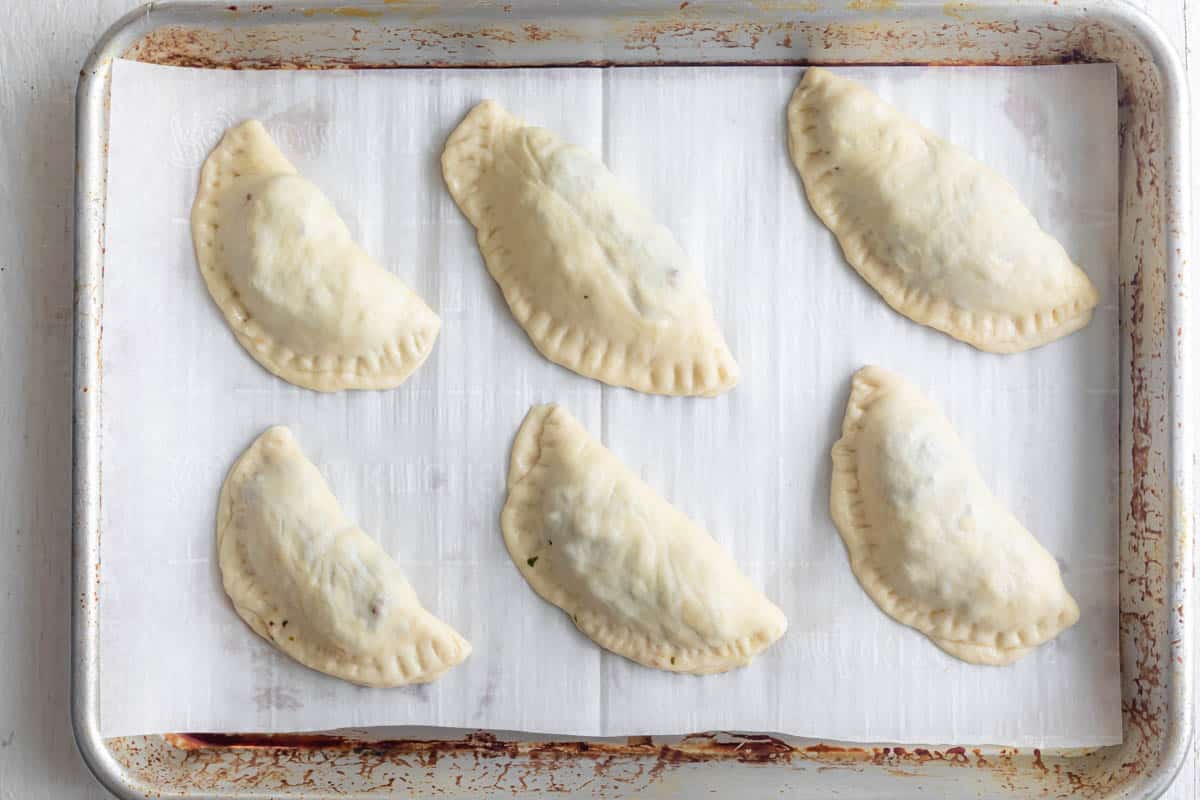 Meat pies on baking dish with parchment paper before baking