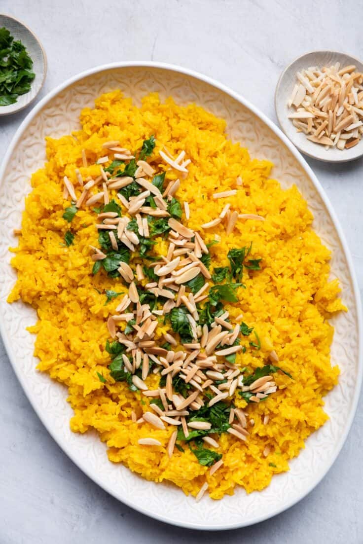 Turmeric rice served in a large platter topped with parsley and almonds