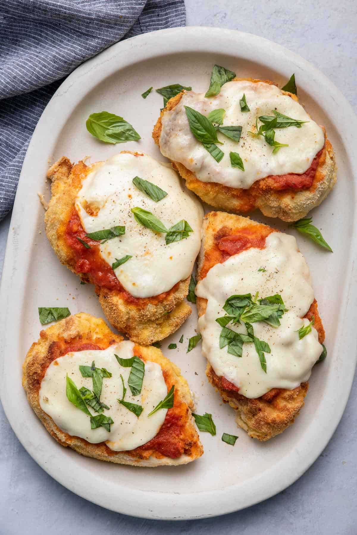 Chicken parmesan on a plate topped with melted mozzarella cheese and basil