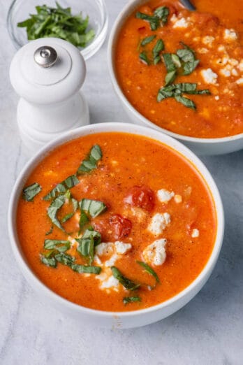 Two bowls of baked feta soup topped with basil