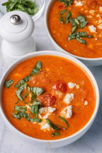 Two bowls of baked feta soup topped with basil