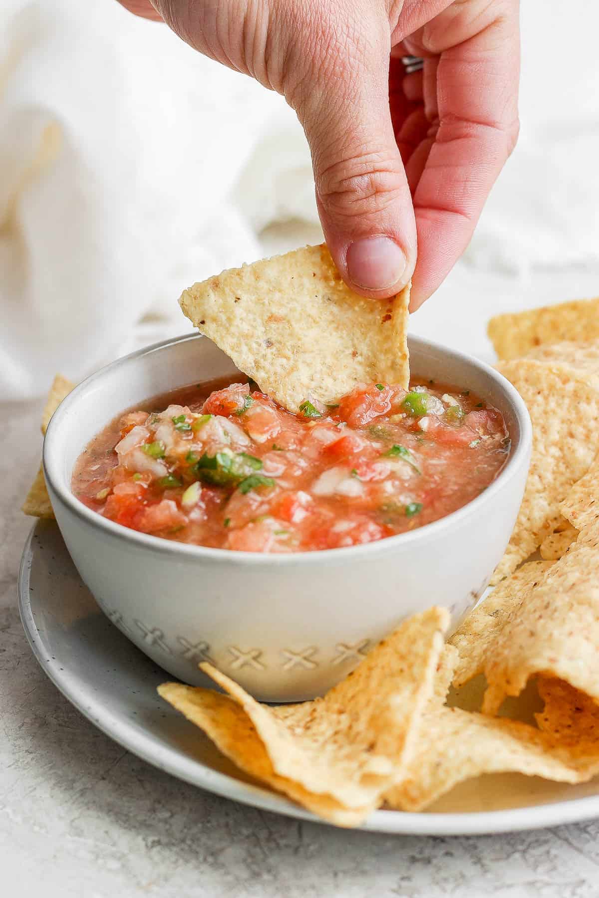 Chip dipping into homemade salsa in a small bowl
