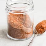 Homemade taco seasoning in a glass jar with a spoon on the side