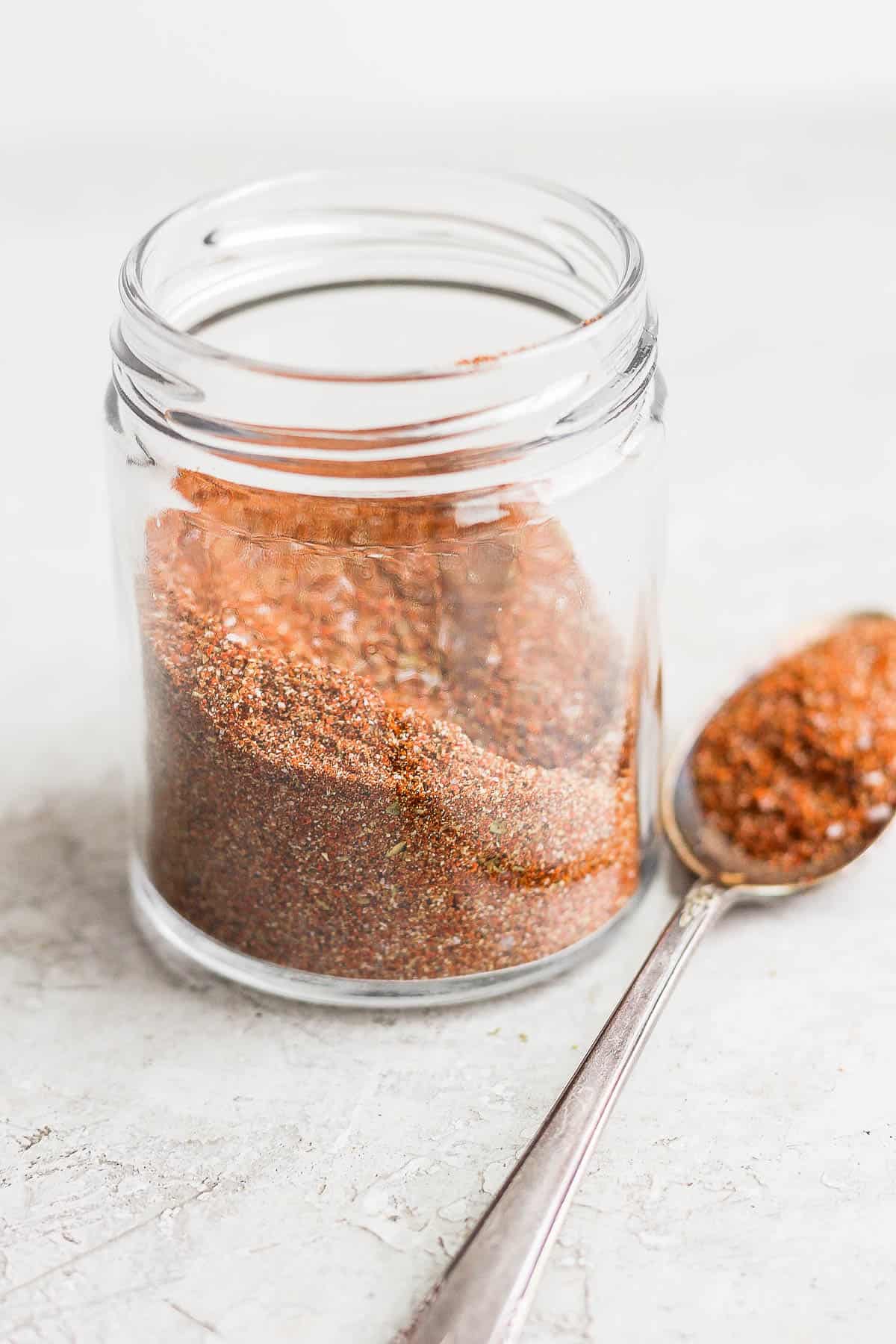 Homemade taco seasoning in a glass jar with a spoon on the side