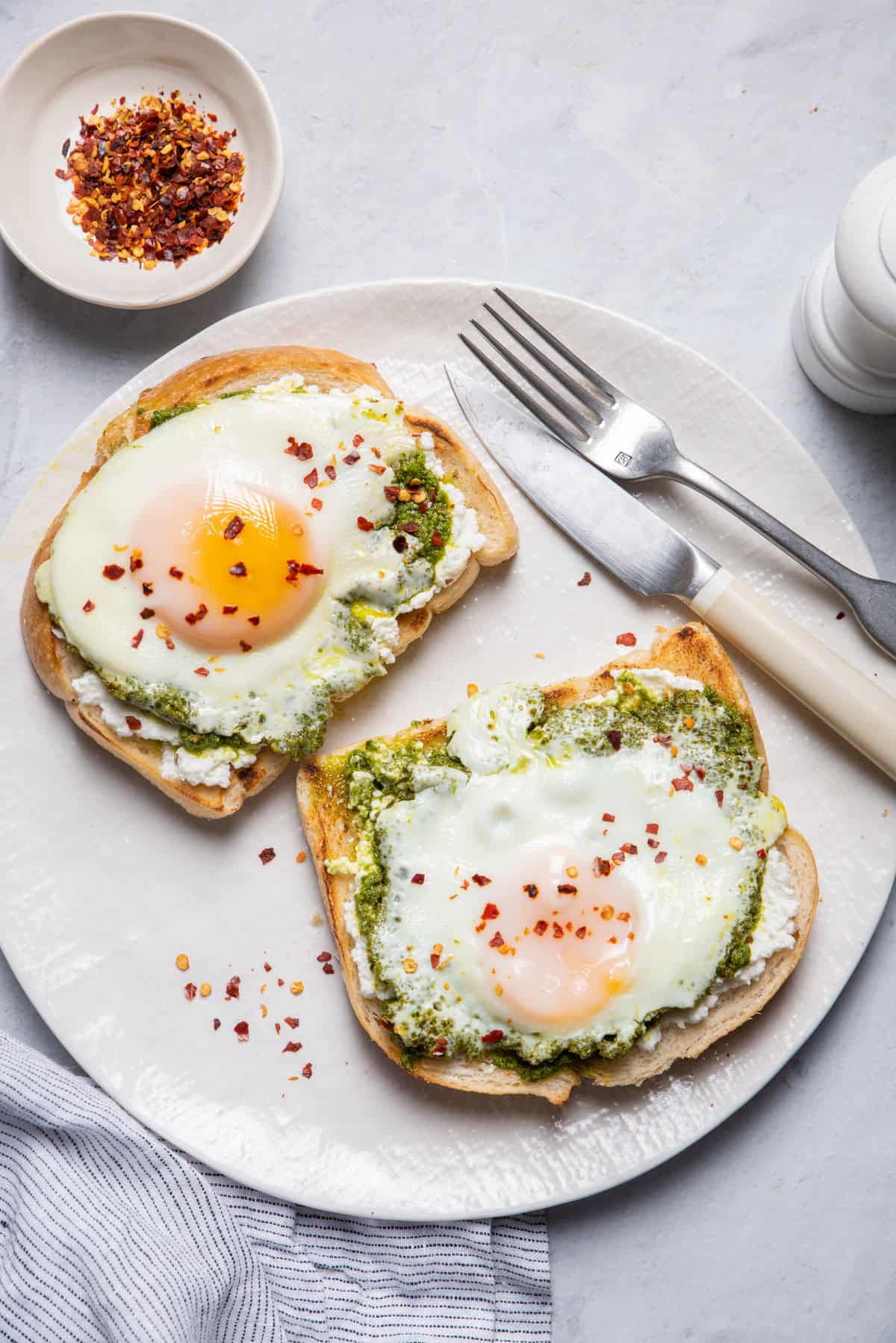 Plate with two pieces of bread topped with pesto eggs with fork and knife on plate