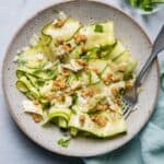 Large bowl of zucchini salad made with zucchini ribbons with blue towel and serving ware in bowl