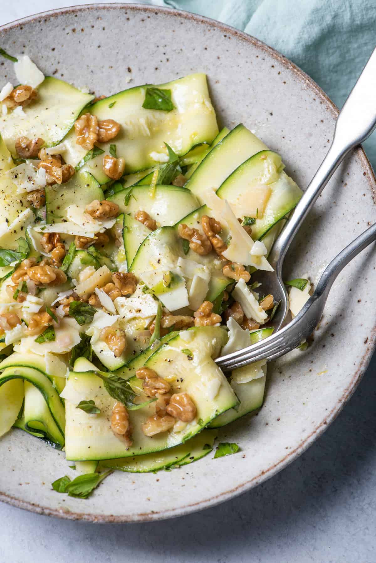 Close up shot of the bowl of zucchini salad with fork and spoon scooping some up