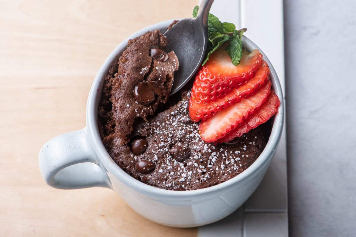 A chocolate mug cake with strawberries on top and a spoon taking out one bite.