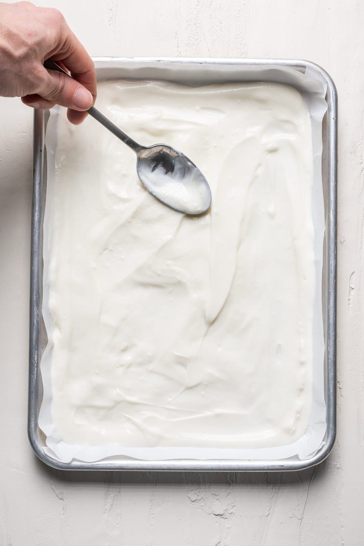 Pouring yogurt into baking dish lined with wax paper.