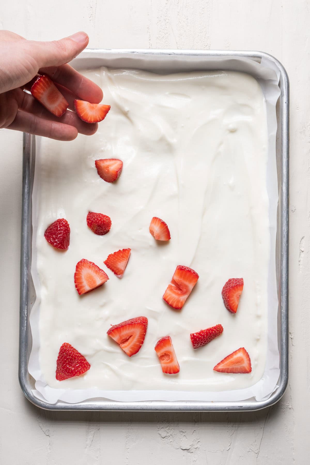 Sprinkling strawberries on top of the yogurt.
