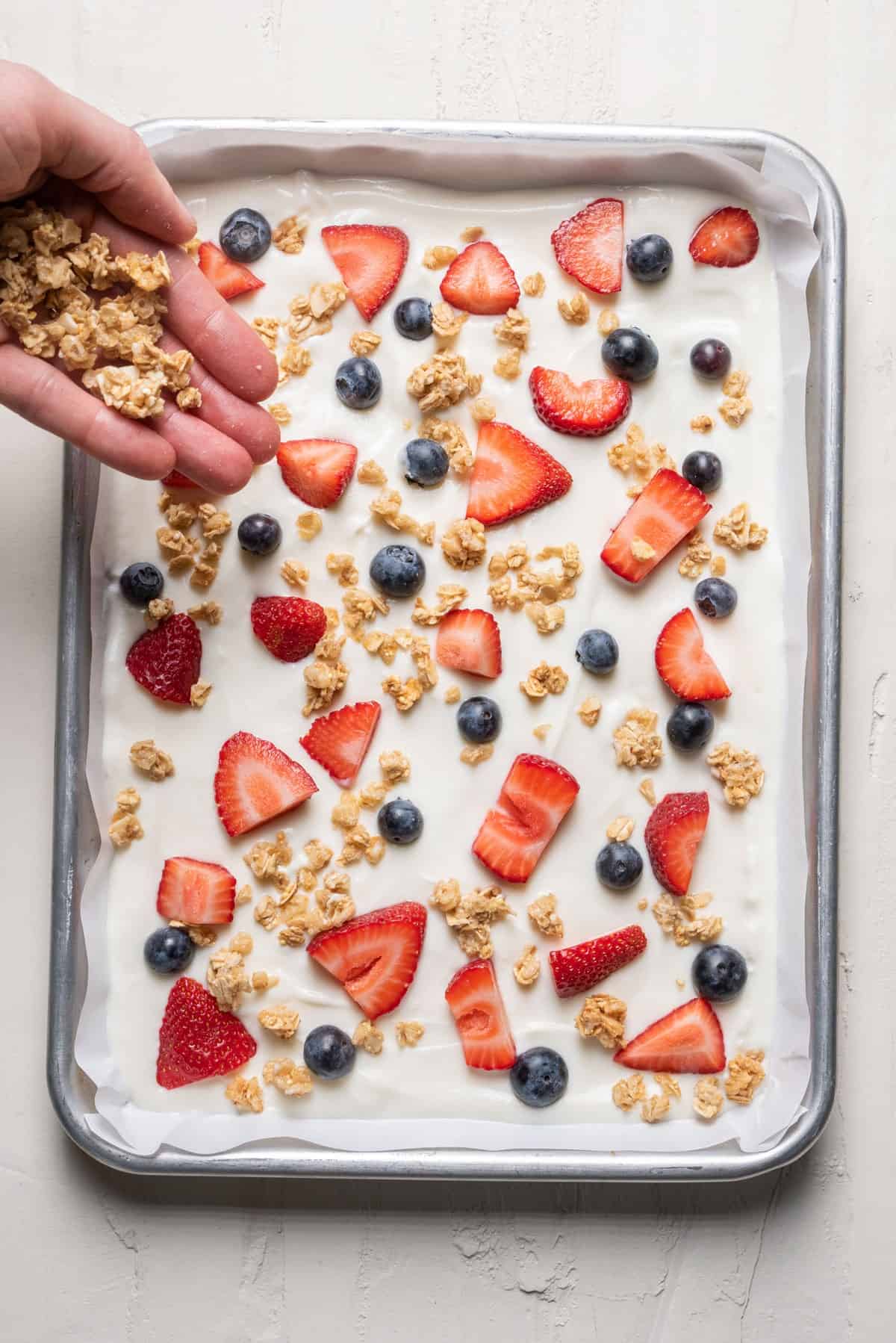 Sprinkling granola on top of the yogurt.