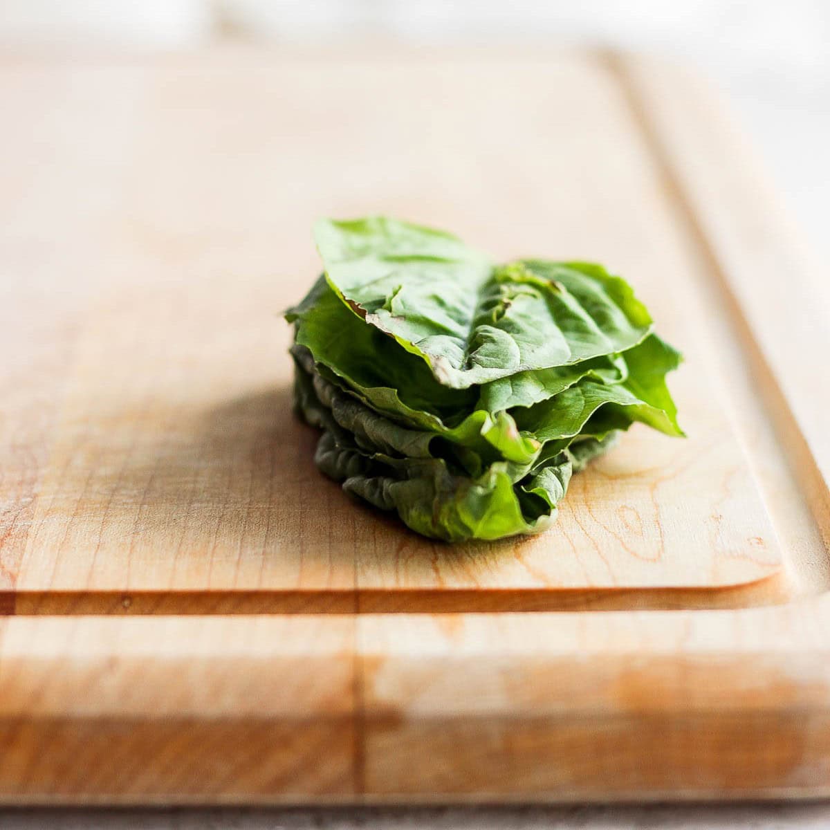 Stack of 5 basil leaves on top of each other on cutting board.