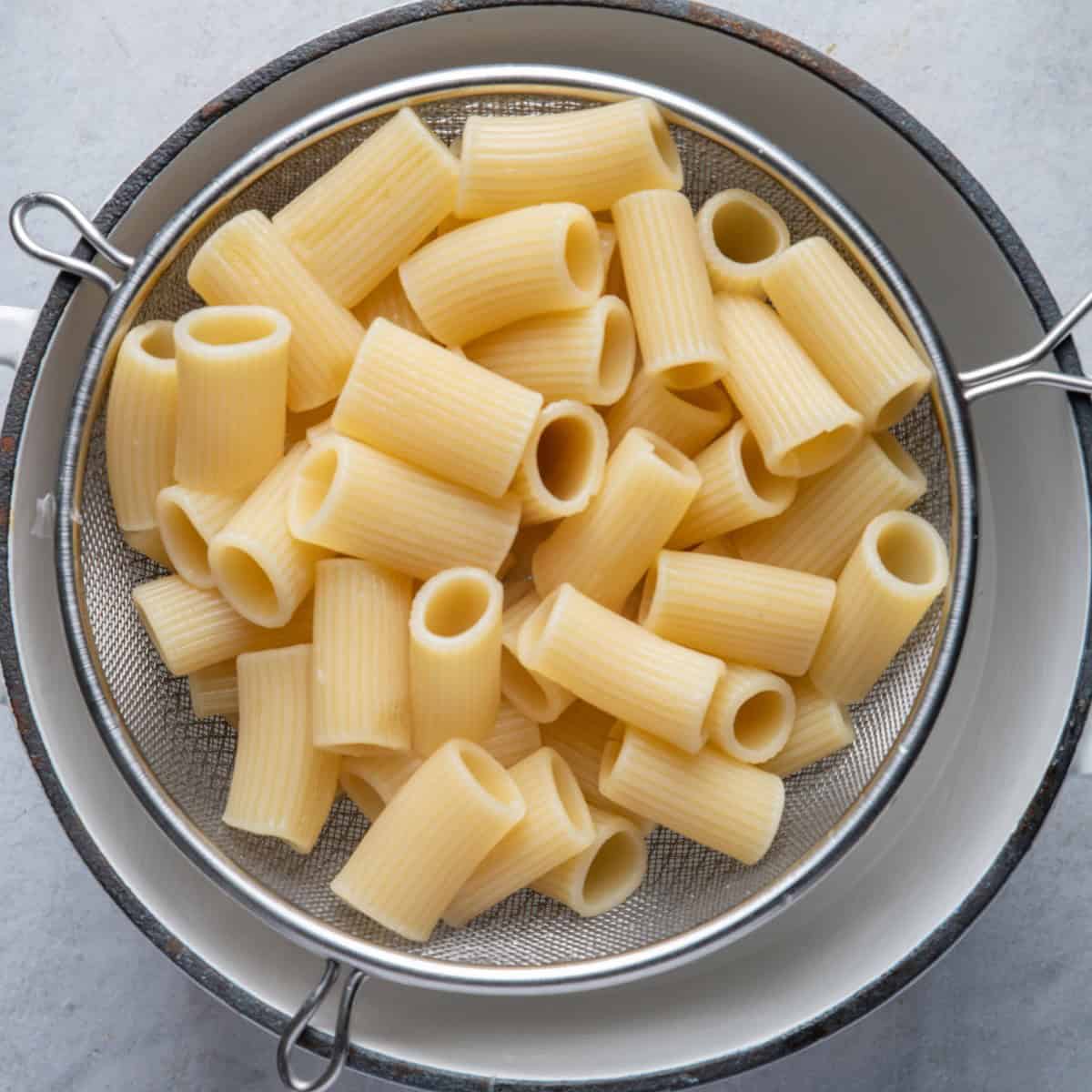 Strainer pulling out cooked pasta from pot.