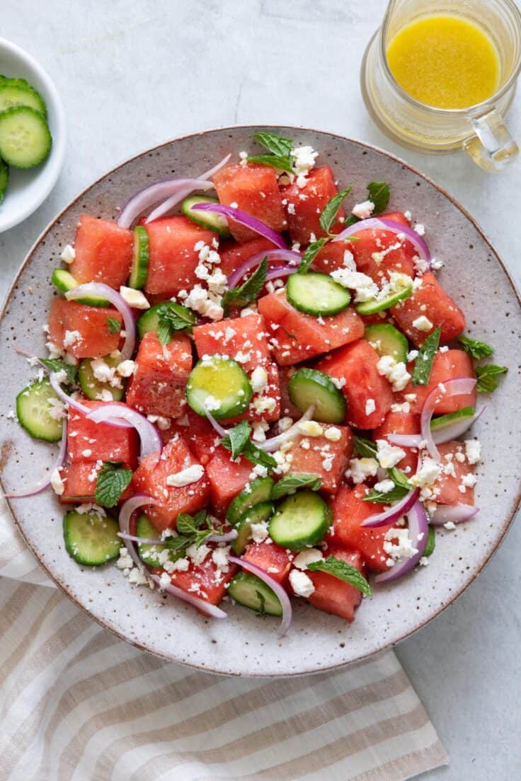 Watermelon feta salad served in a large bowl with cucumbers and onions.