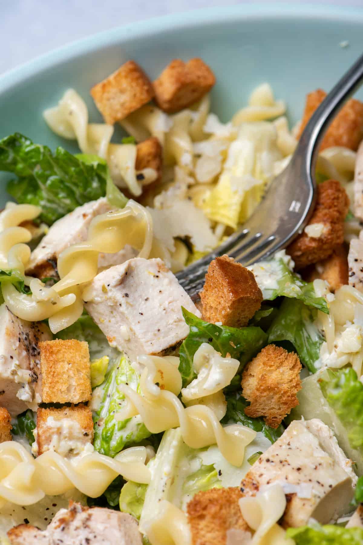 Bite taking bite of chicken caesar pasta salad