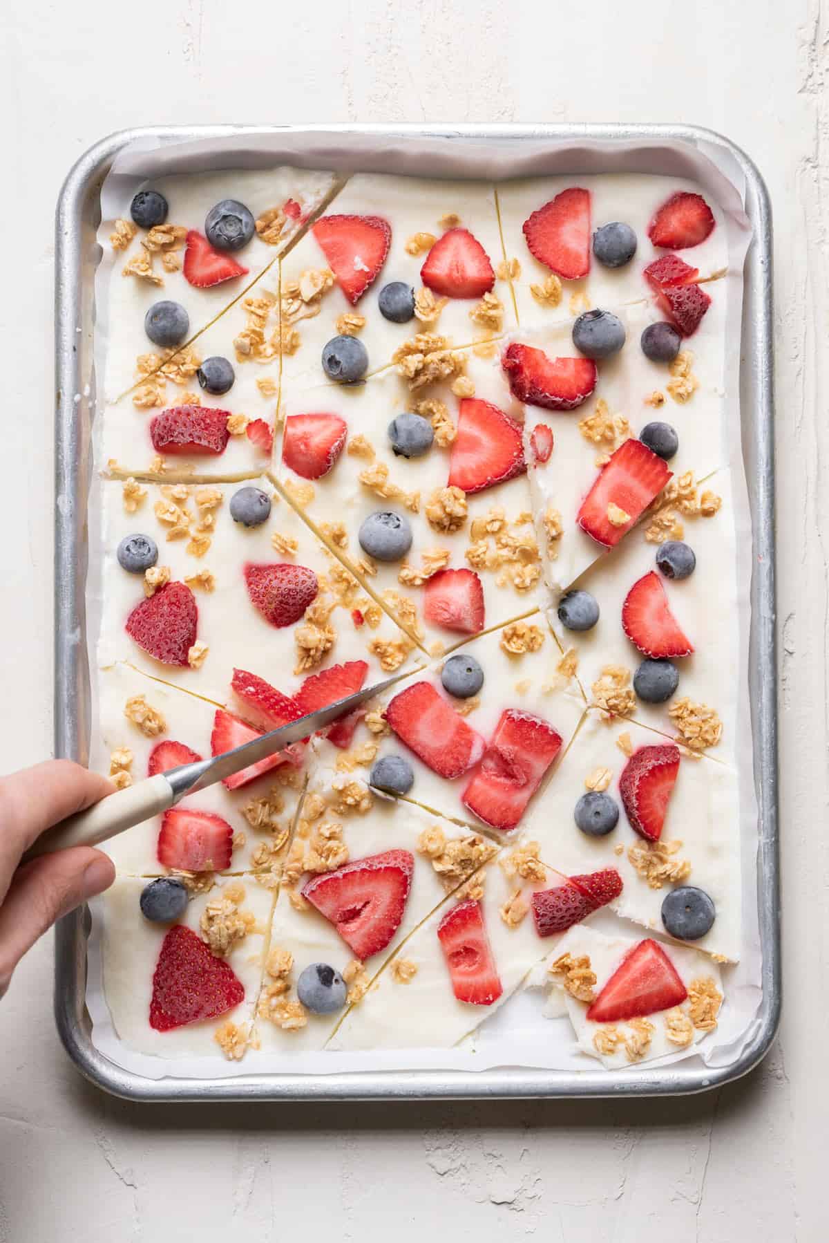 Frozen yogurt bark with fruits and granola getting cut