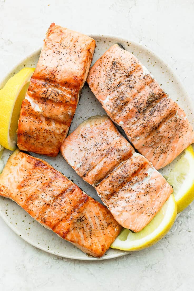 Plate of 4 salmon fillets grilled served with lemon wedges