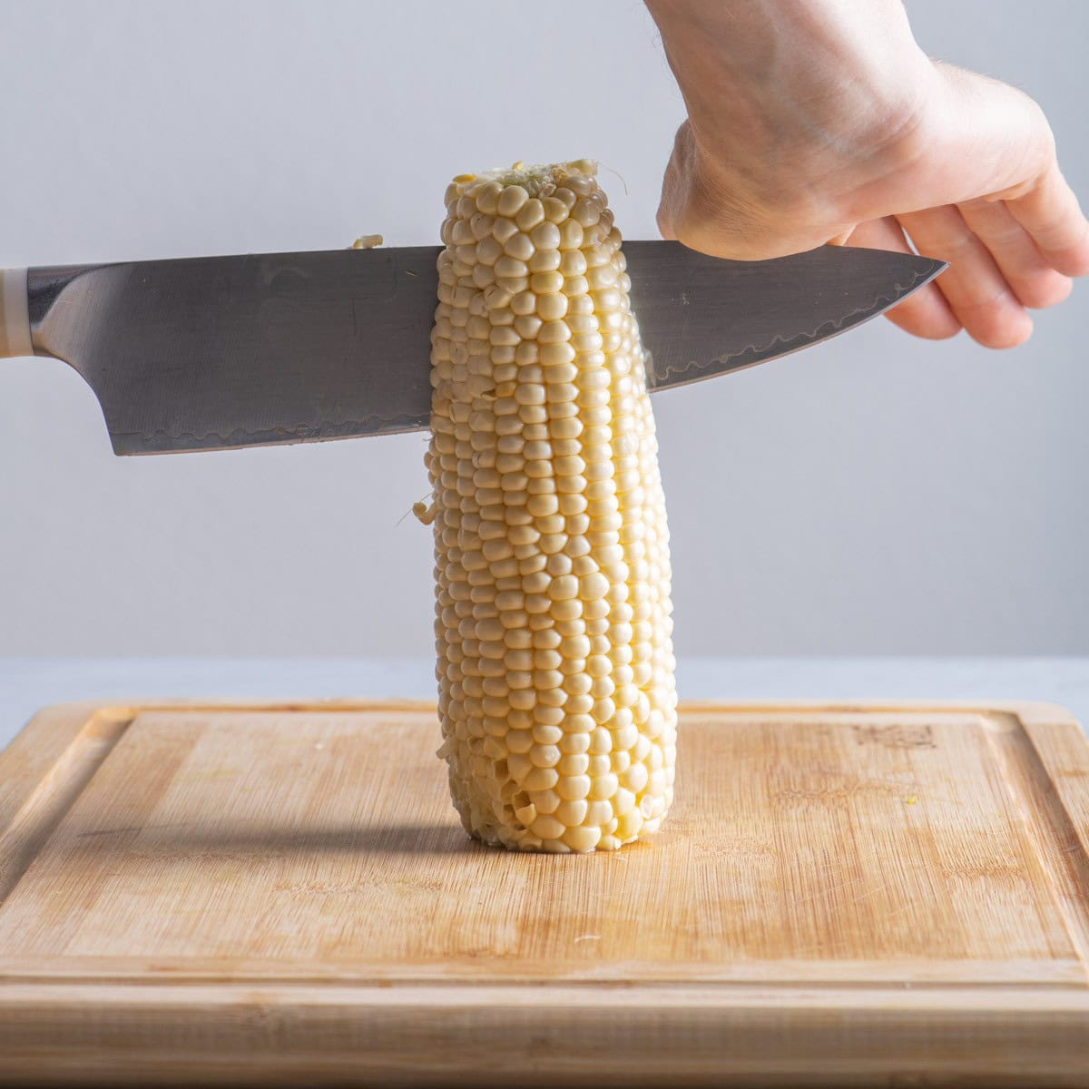 Corn on cutting board with knife cutting down vertically.