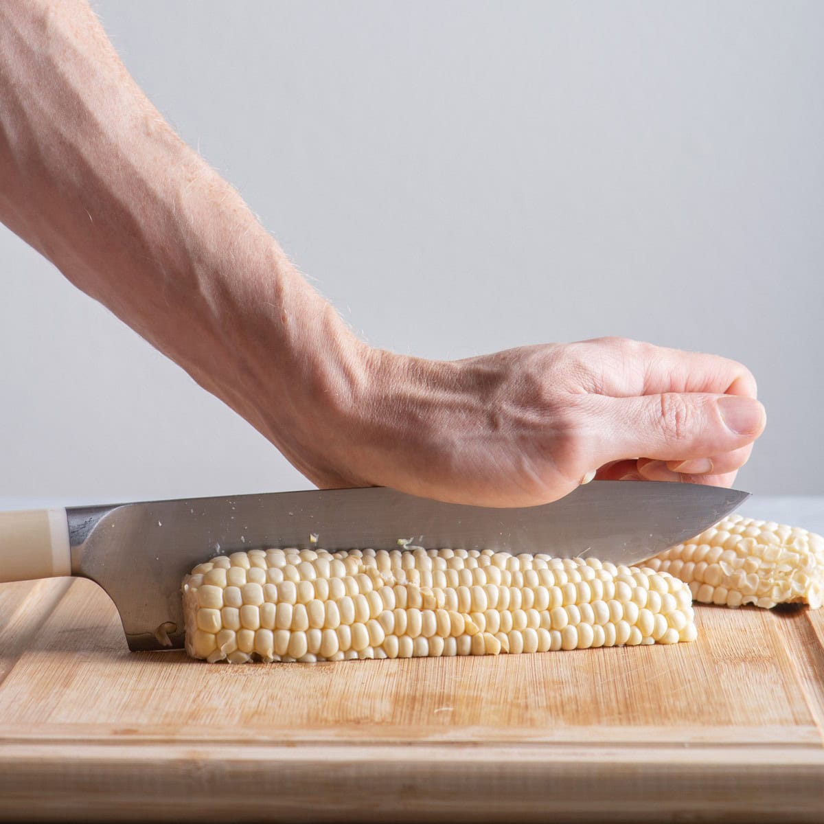 Corn on cutting board cutting into quarters.