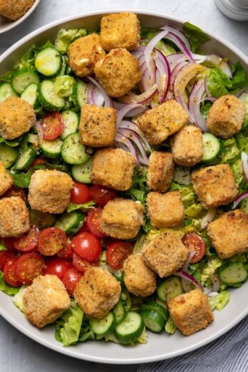 A bowl of feta salad with more ingredients nearby.