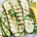 Grilled zucchini with lemon and garnish stacked on a plate.