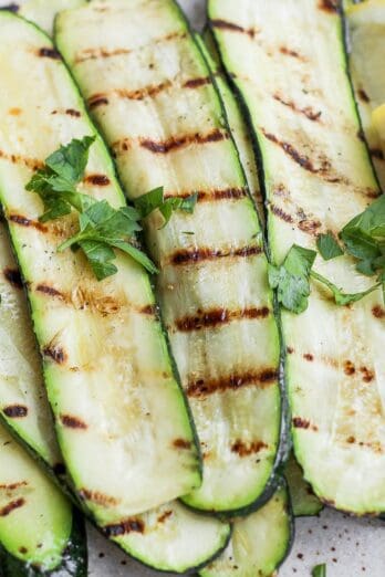 Grilled zucchini with lemon and garnish stacked on a plate.