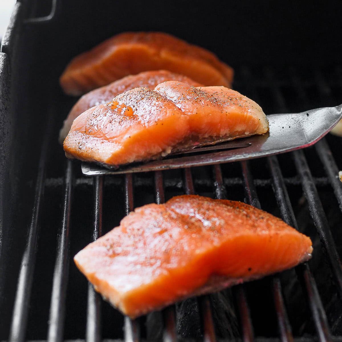 4 fillets of salmon on the grill with one of them getting flipped over to show the skin.