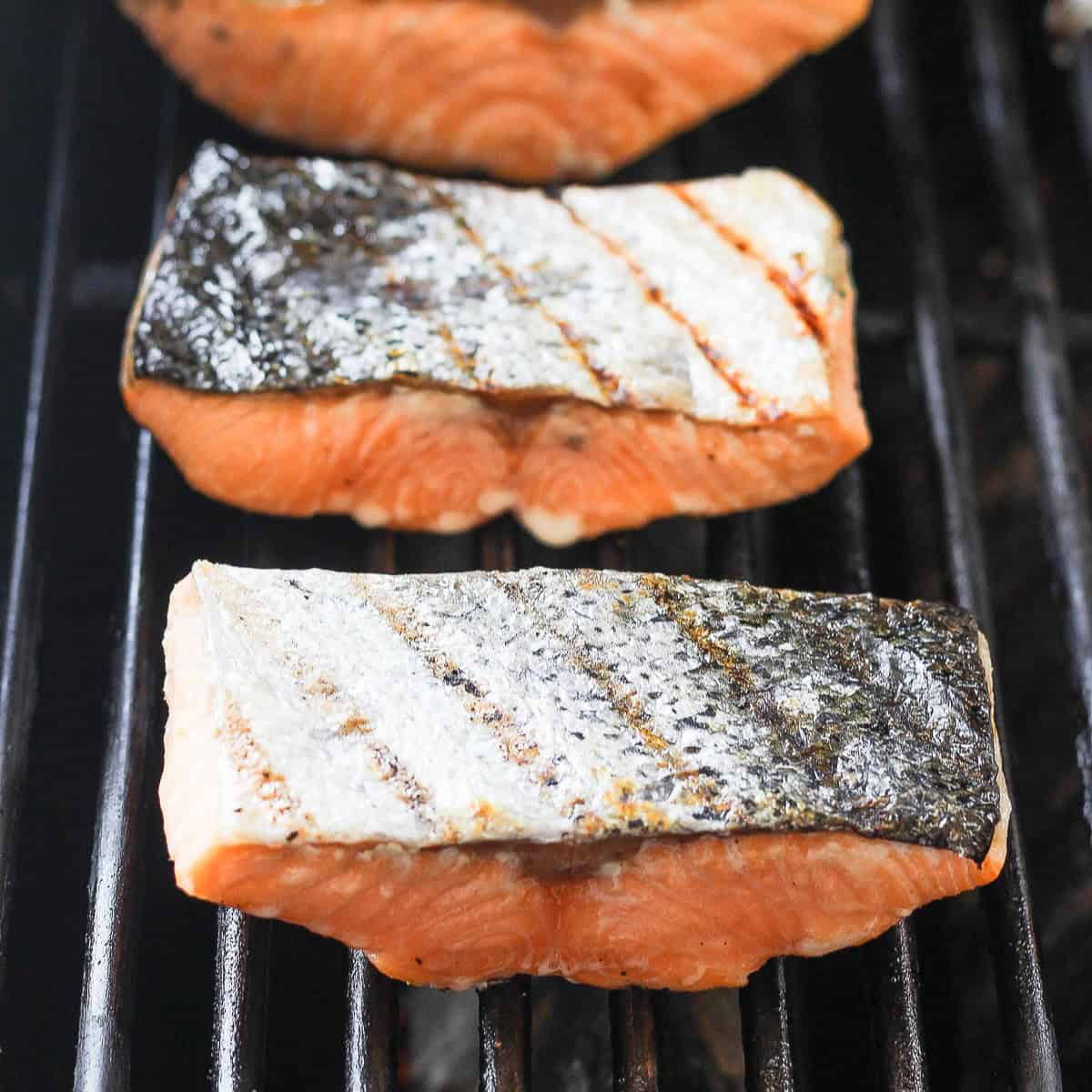 4 fillets of salmon on the grill flipped over to show the grilled skin.