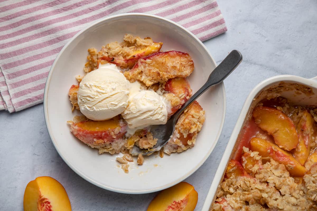 Peach crisp after baking in a bowl served a la mode with vanilla ice cream
