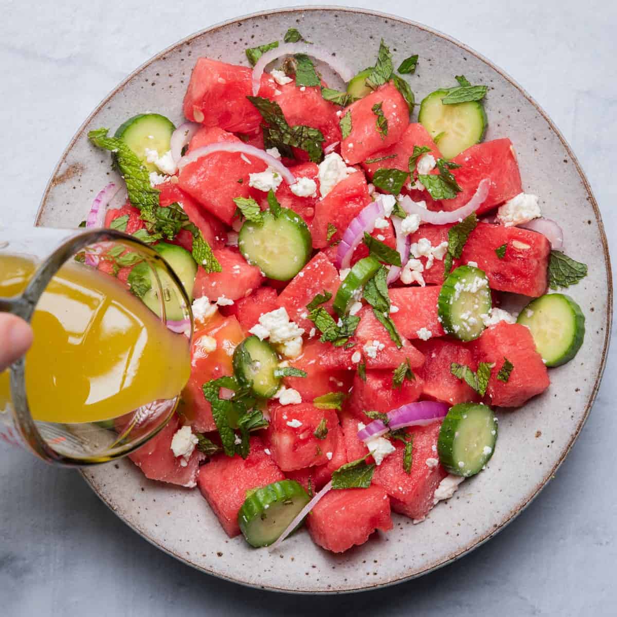 Pouring dressing over watermelon salad.