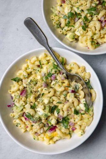 Two bowls of macaroni egg salad with spoon in one bowl