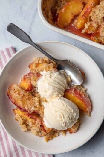 Peach crisp in a bowl served with two scoops of vanilla ice cream